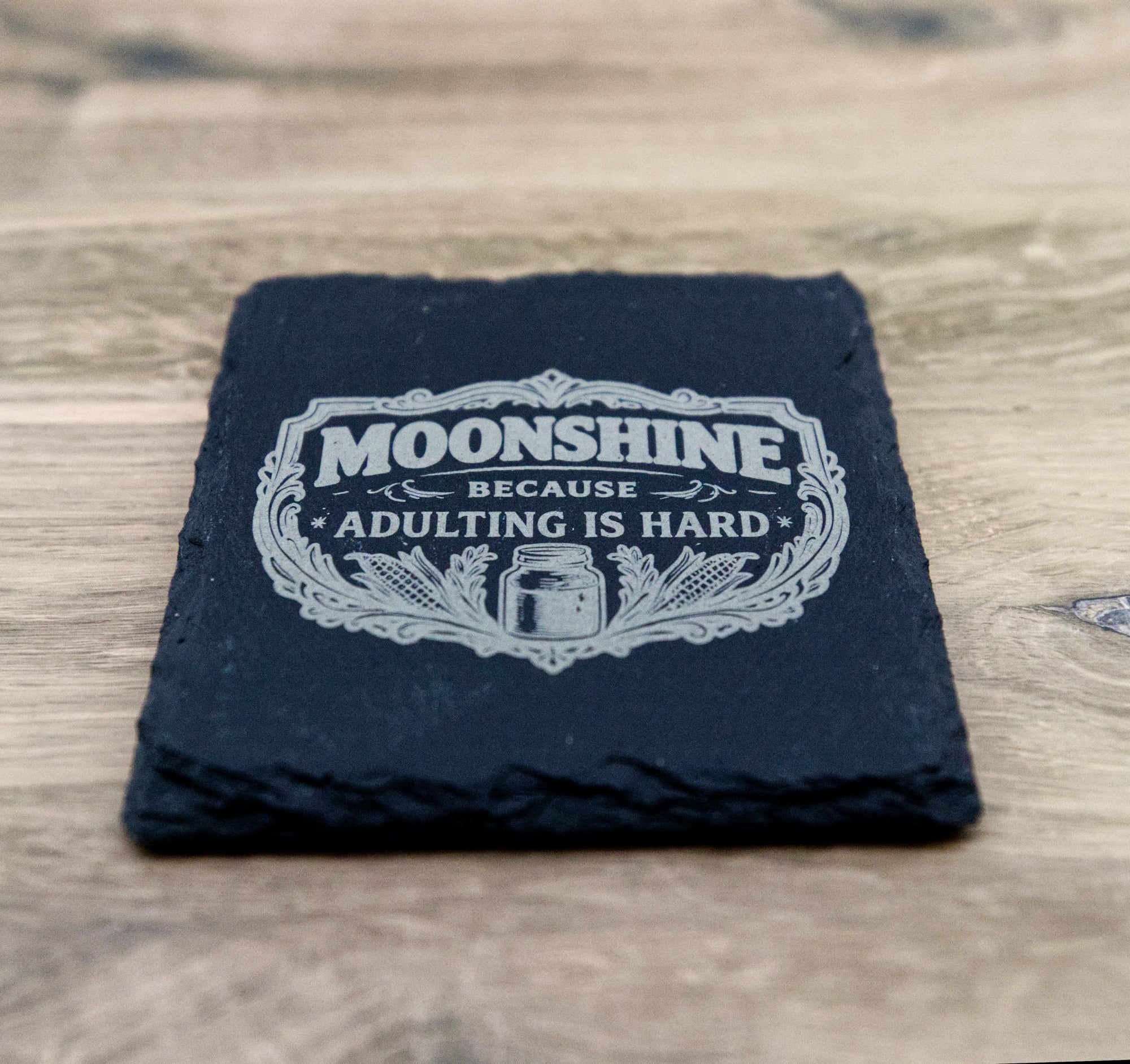 Laser-engraved moonshine slate coaster on a wood surface
